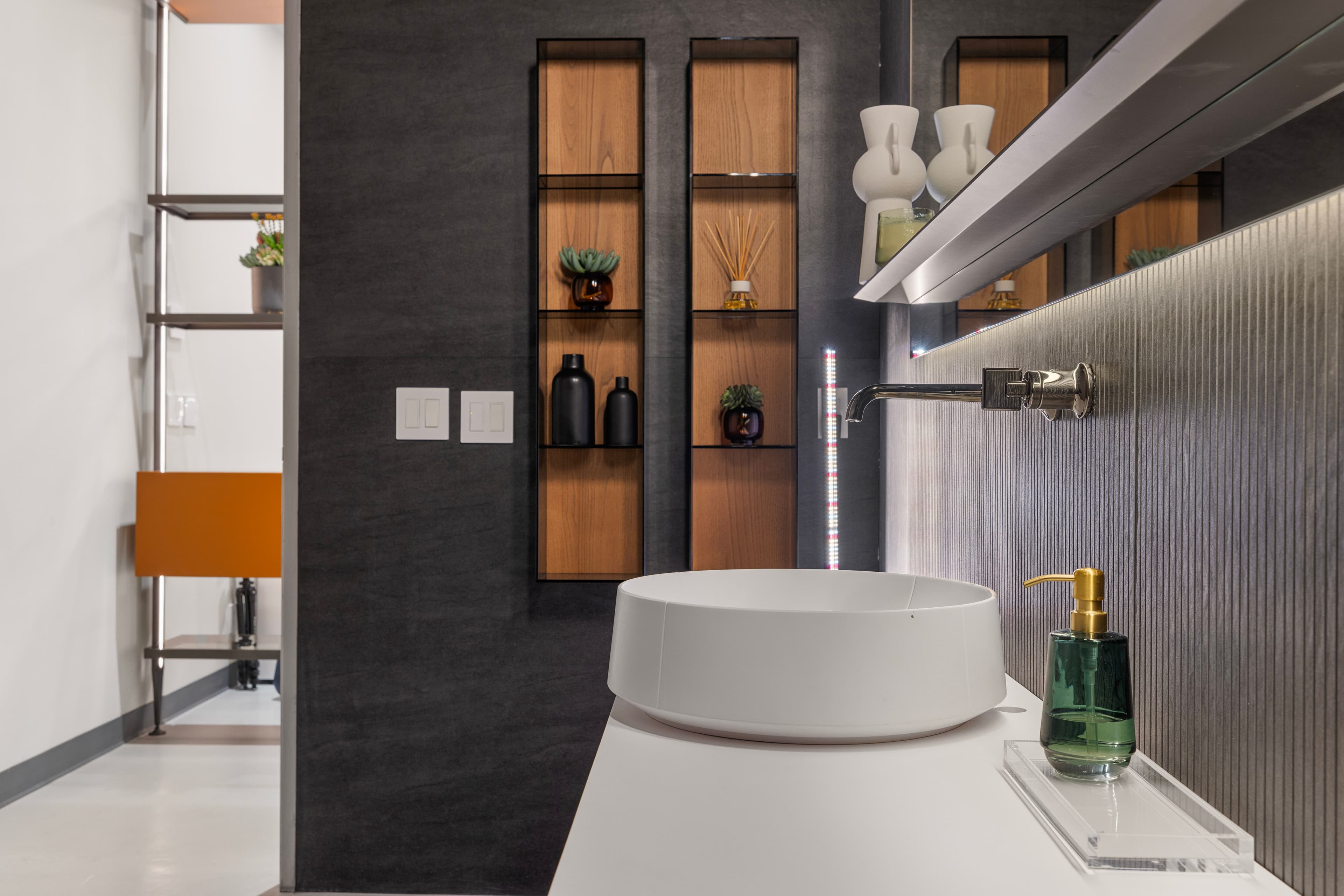 Modern bathroom with a sleek sink, open shelving, and a combination of dark and light tones, featuring organized storage solutions.